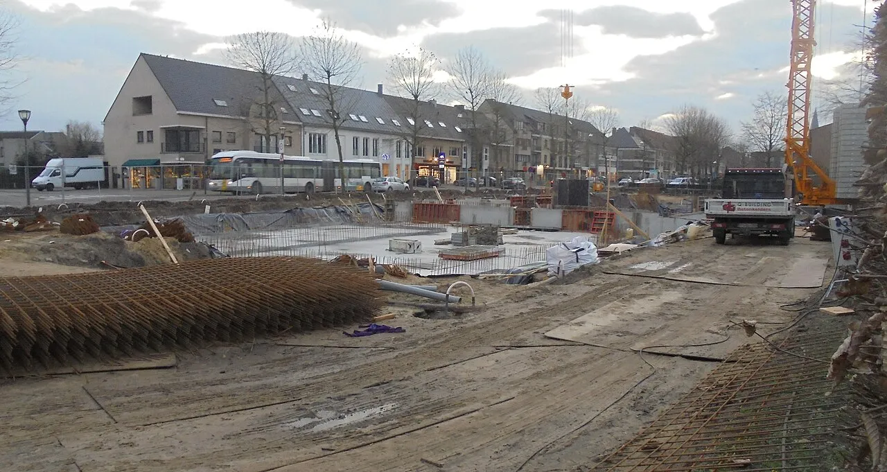 Bouwwerf met steigers en betonwerk bij een nieuwbouwproject in Oost-Vlaanderen, België.